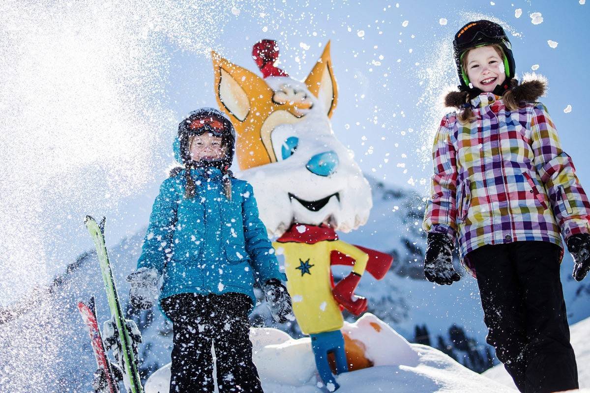 Zwei Kinder mit dem Fuchs-Maskottchen im aufstiebenden Schnee